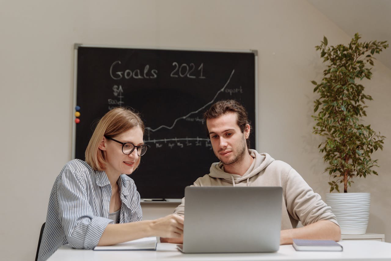Two coworkers collaborating on 2021 goals in a modern office setting with a laptop.