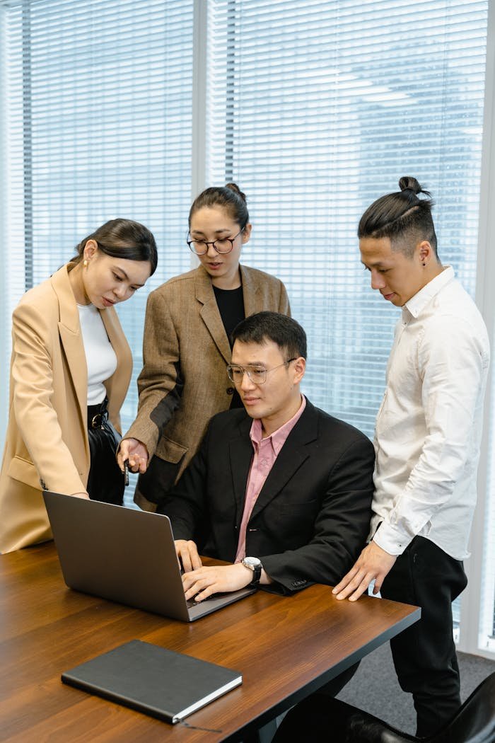 A diverse team collaborates around a laptop in a modern office setting.